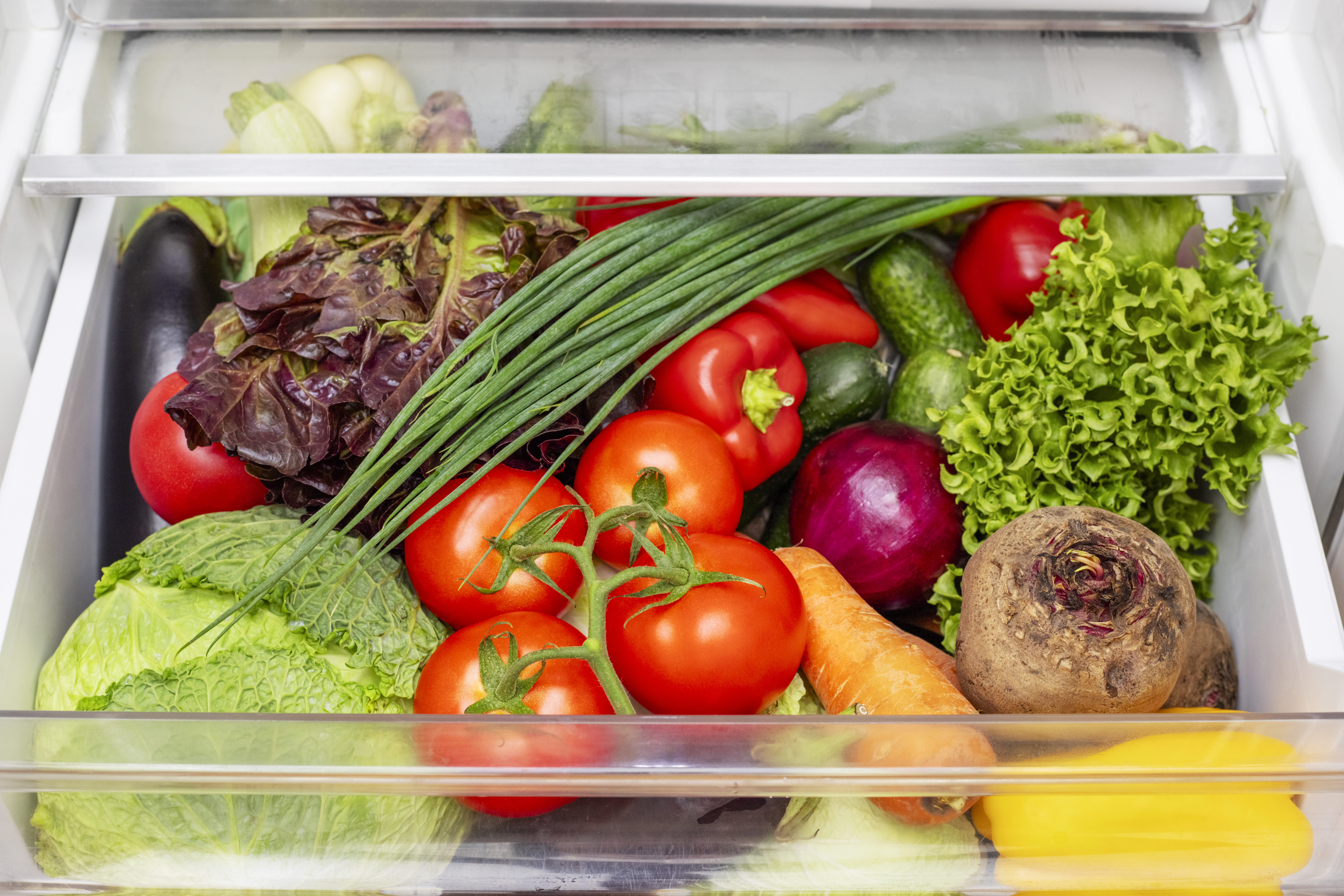 Vegetable compartment of the refrigerator full of fresh vegetables. Open fridge, drawer filled with fresh vegetables.