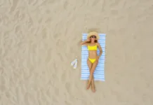 Kopalke in brisača po plaži: večina ljudi dela isti dve napaki. Tudi vi? Woman sunbathing on beach towel at sandy coast, aerial view. Space for text