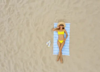 Kopalke in brisača po plaži: večina ljudi dela isti dve napaki. Tudi vi? Woman sunbathing on beach towel at sandy coast, aerial view. Space for text