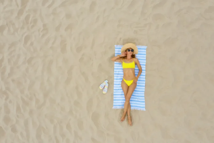 woman-sunbathing-on-beach-towel-at-sandy-coast-aerial-view-space-for-text-stockpack-istock Woman sunbathing on beach towel at sandy coast, aerial view. Space for text