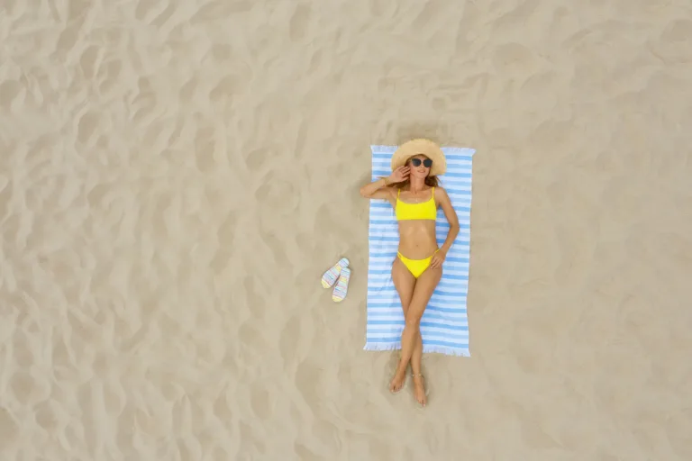 Woman sunbathing on beach towel at sandy coast, aerial view. Space for text