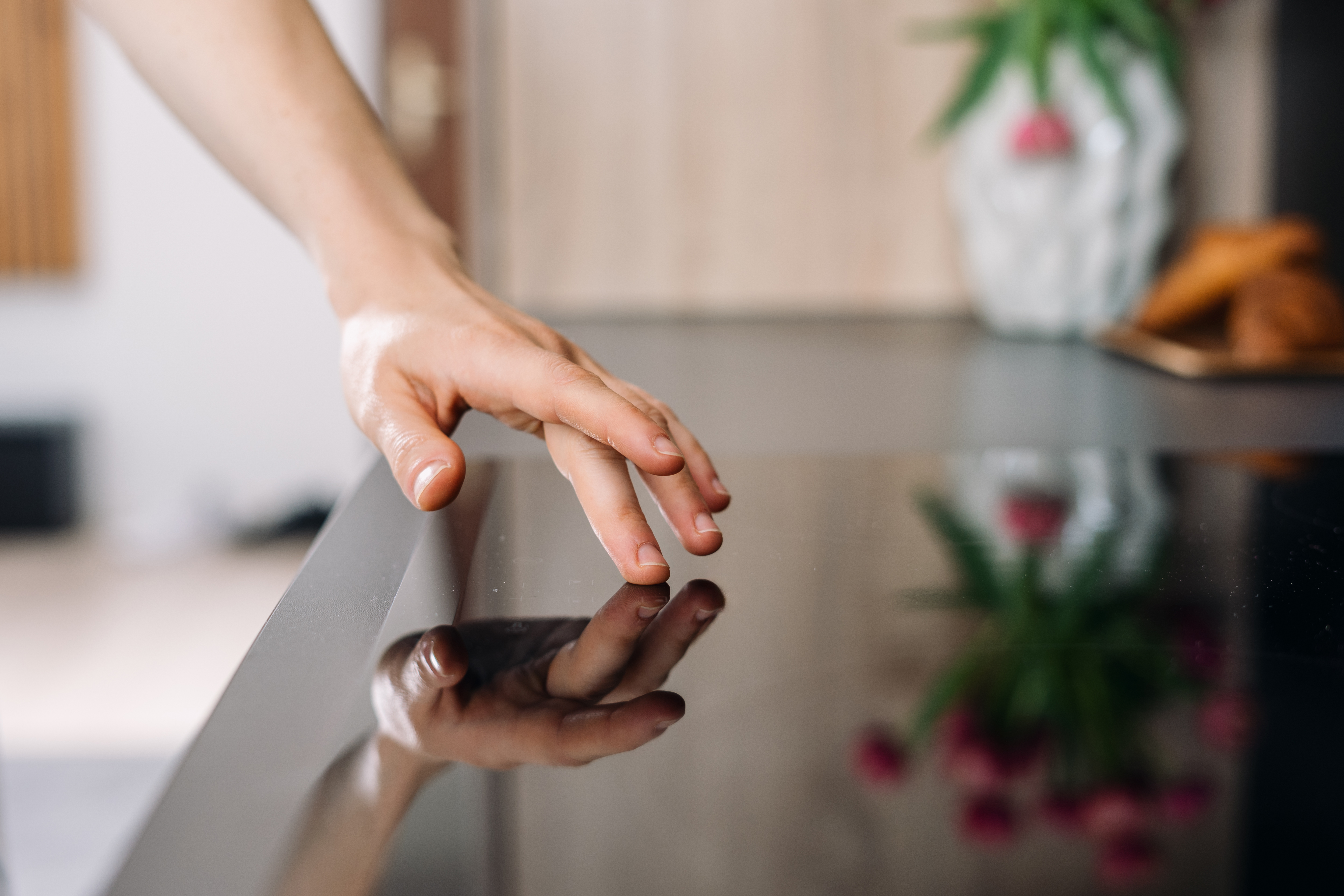 Woman touches surface of a electric stove, choose temperature on burner for cooking. Household appliances built into a kitchen counter, reflecting vibrant plants and decor in a stylish domestic space