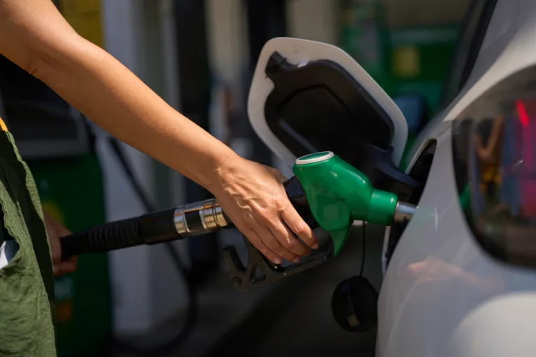 Close up of a woman's hand holding a gas pump, refueling her car at a gas station