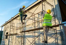 Cena gradbenih del v primerjavi z lanskim letom zrasla za kar 23 odstotkov Construction workers in uniform and safety equipment working on scaffolding at building site.