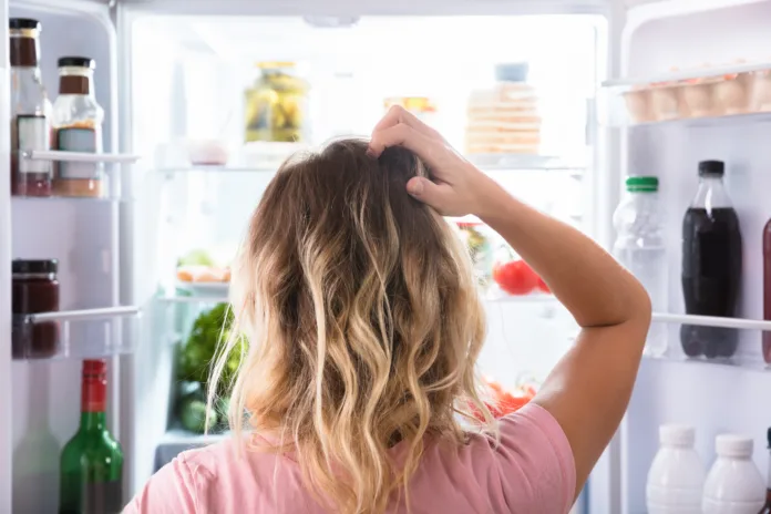 rear-view-of-a-confused-woman-looking-in-open-refrigerator-at-home-stockpack-istock Rear View Of A Confused Woman Looking In Open Refrigerator At Home