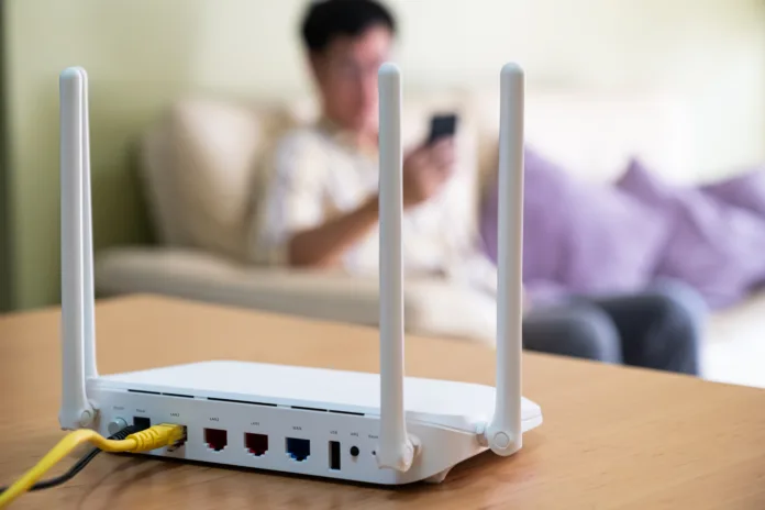 Selective focus at router. Internet router on working table with blurred man using smart phone at the background. Fast and high speed internet connection from fiber line with LAN cable connection.