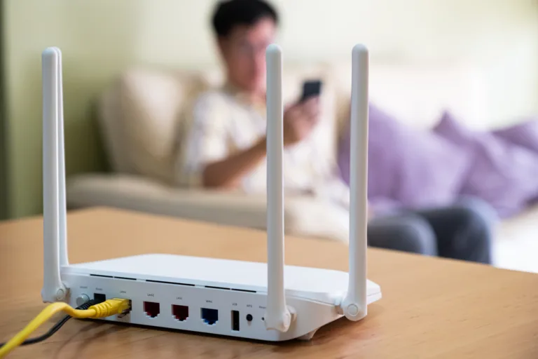Selective focus at router. Internet router on working table with blurred man using smart phone at the background. Fast and high speed internet connection from fiber line with LAN cable connection.