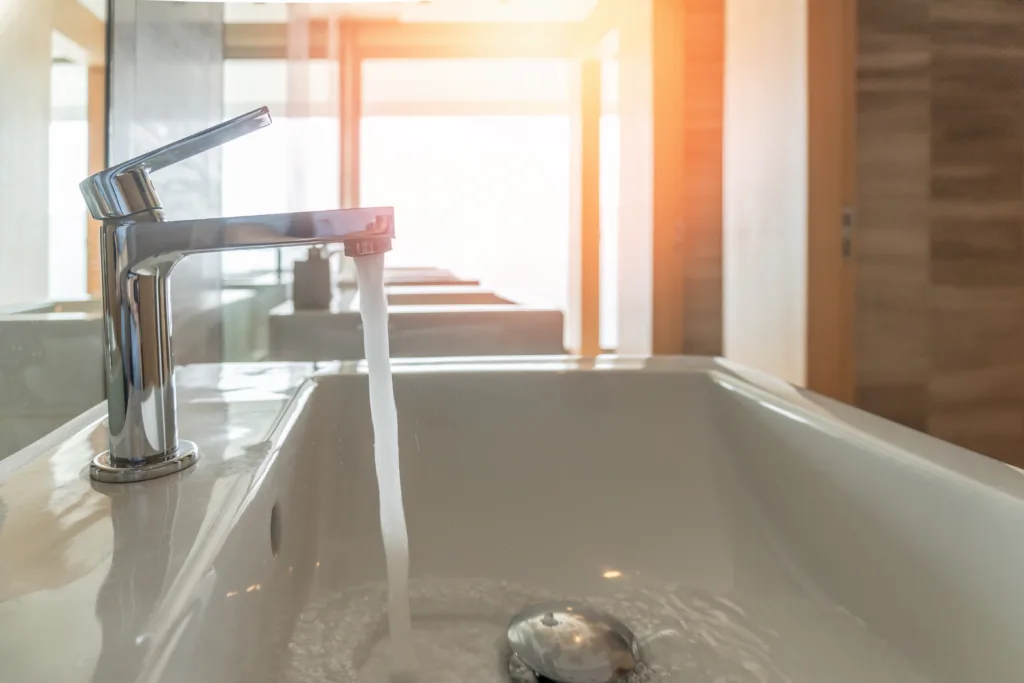 Tap water running wastage from faucet over hand washing sink, ceramic basin in water closet, public wc room or school bathroom for saving ecological and environmental conservation awareness concept