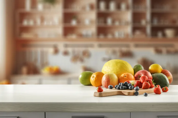 blurred-kitchen-interior-and-fresh-fruit-on-wooden-cutting-board-on-white-countertop-and-space-for-food-and-drink-and-products-and-objects-natural-daily-light-coming-through-the-window-stockpack-istock Blurred kitchen interior and fresh fruit on wooden cutting board on white countertop and space for food and drink and products and objects. Natural daily light coming through the window.