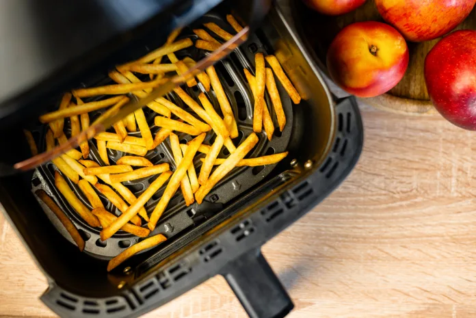 Delicious cooked potato chips frying in a modern kitchen household appliance container next to apples