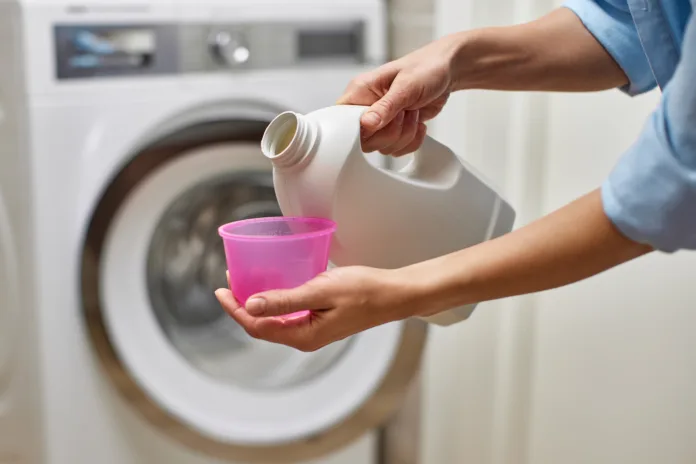 female-hand-pours-liquid-transparent-laundry-detergent-or-conditioner-into-plastic-cap-against-blurred-washing-machine-stockpack-istock female hand pours liquid transparent laundry detergent or conditioner into plastic cap against blurred washing machine.
