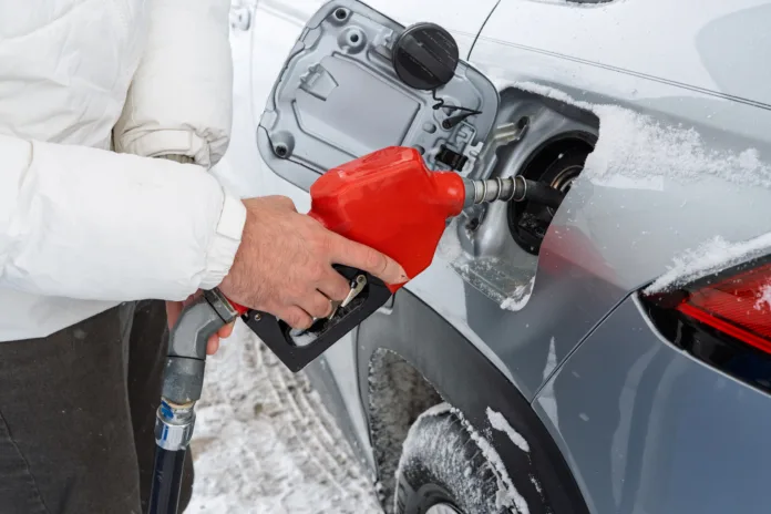 Man holding fuel nozzle while refueling car at gas station. Close-up view of refueling process at gas station with man’s hands During winter and snowing