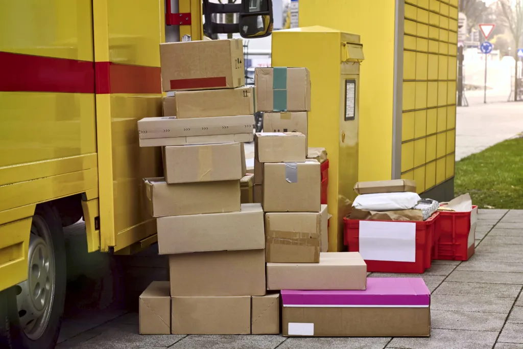 Stack of parcels next to a delivery van are standing on the sidewalk.