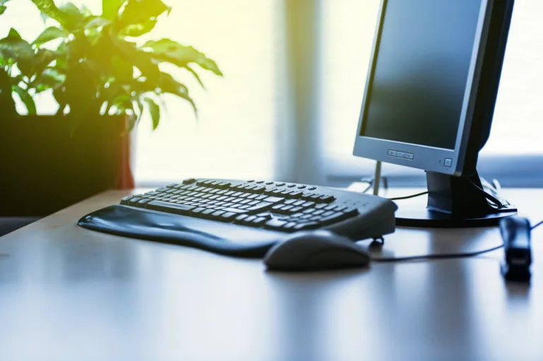 Personal computer on a desk in bright modern office lit by yellow sun coming from the window