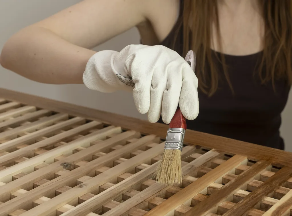 Woman brushes finish onto a wooden storage table. Close up of furniture care with gloves and a paintbrush. Home maintenance and wood restoration concept.